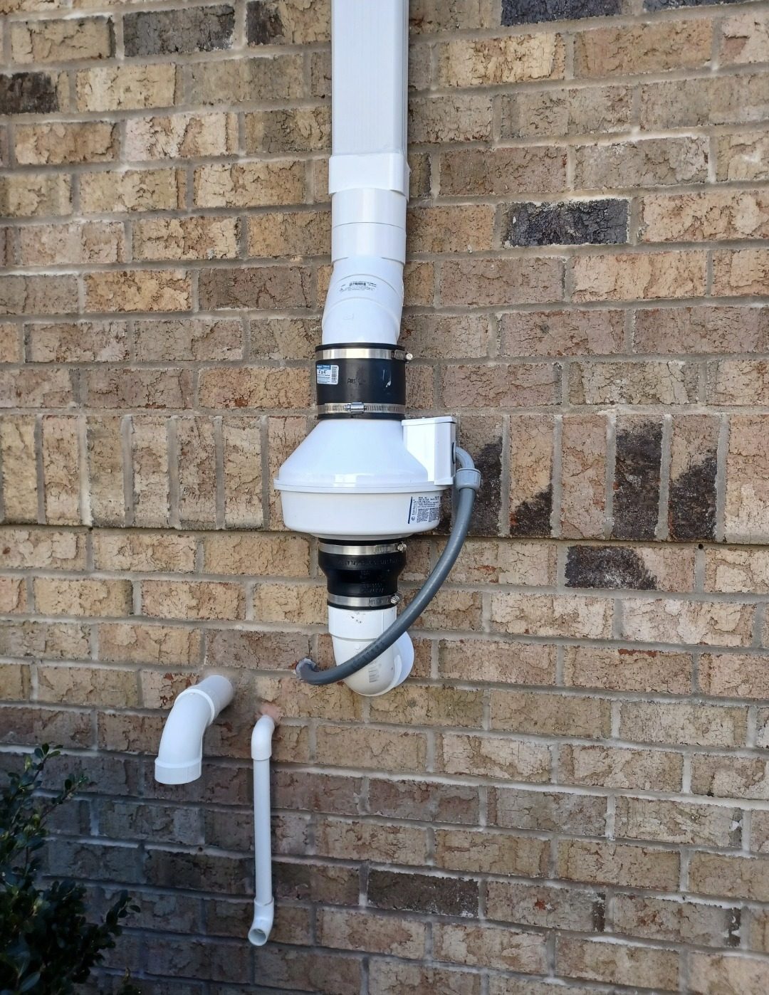 Radon mitigation fan and sealed pipe on a brick exterior wall